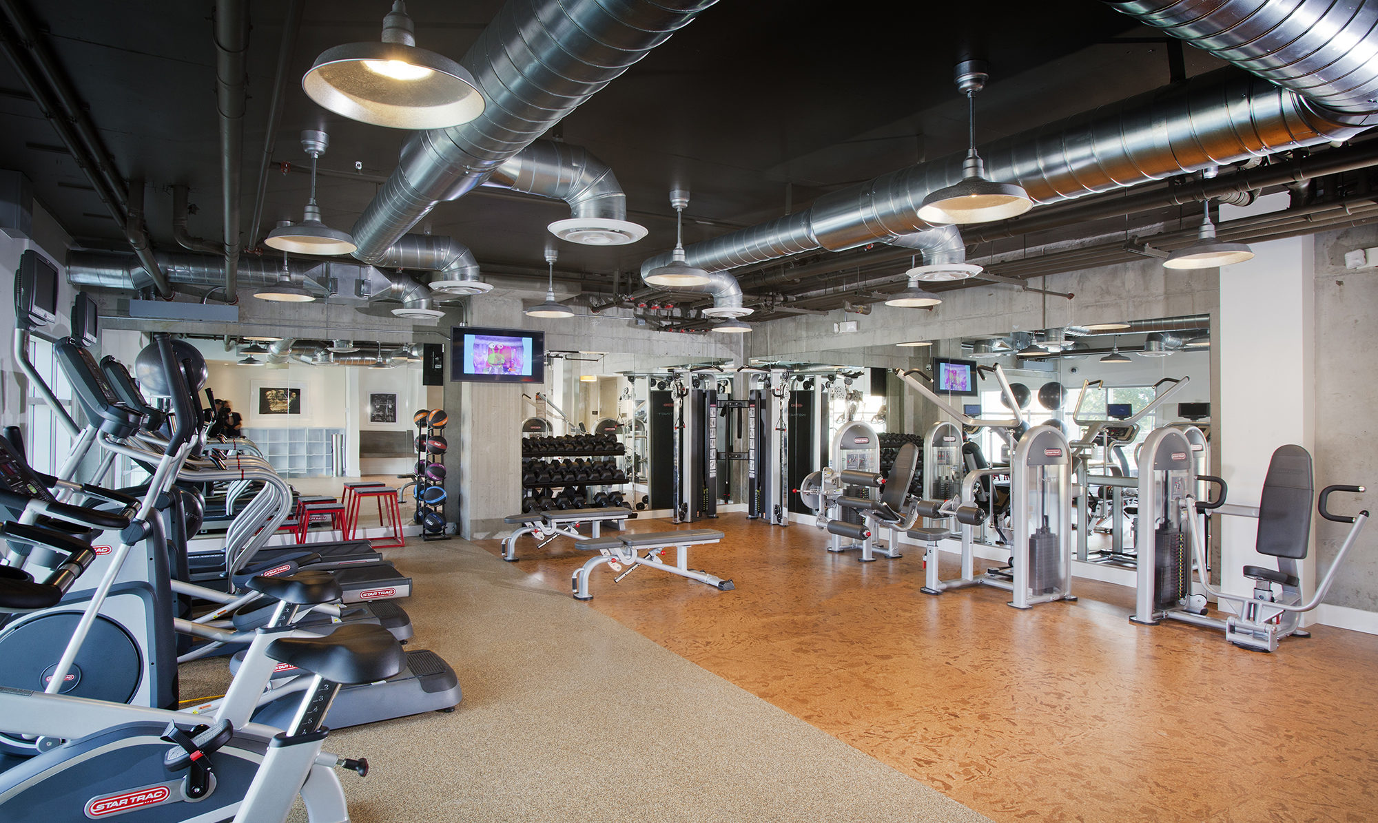 Gym with concrete walls surrounded by mirrors with a variety of workout equipment.