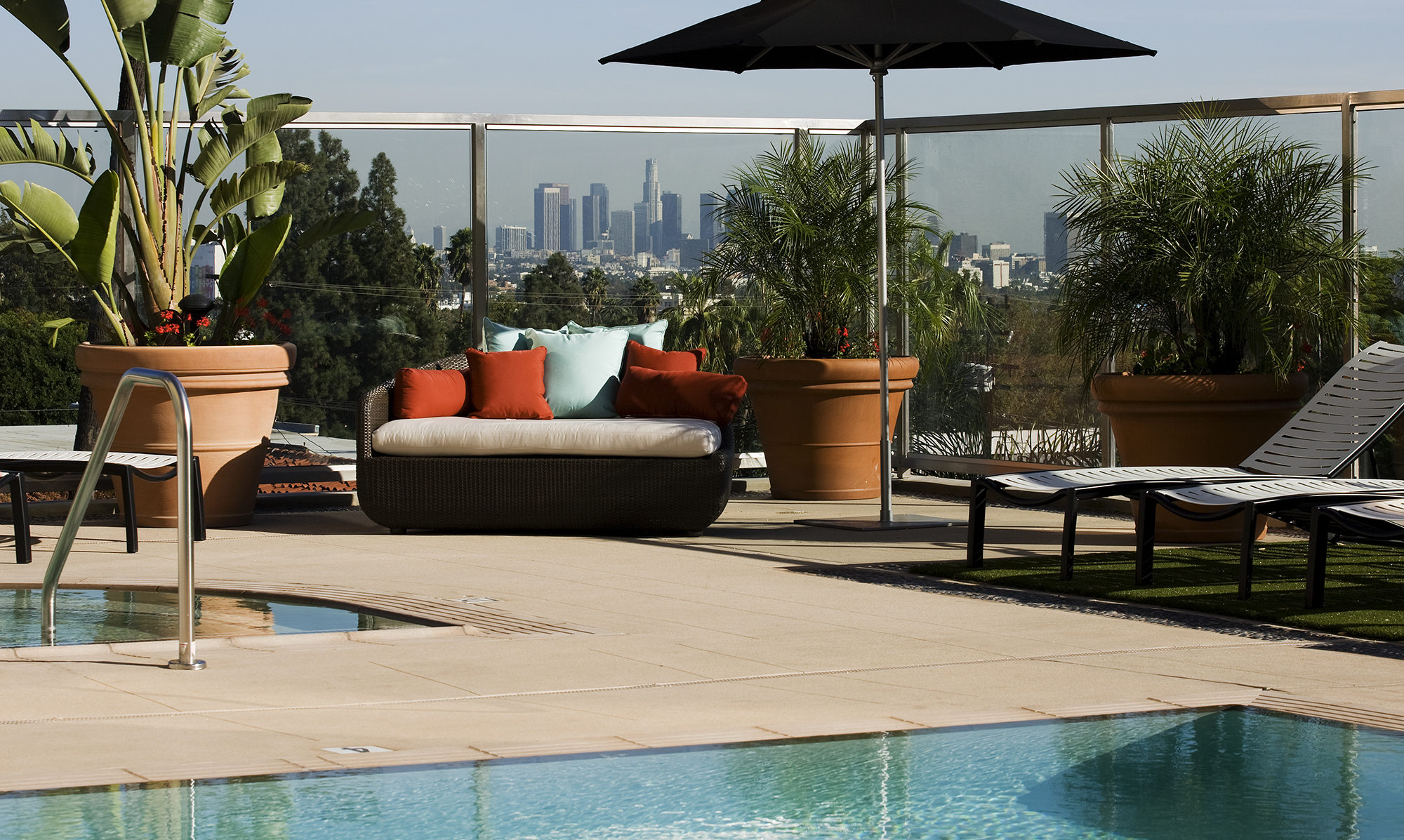 Pool area with umbrella, seating and hot tub looking over city.