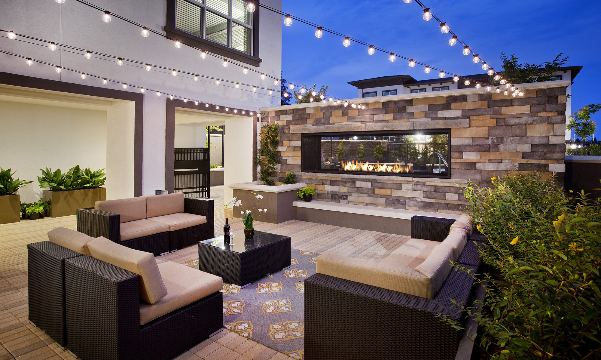 Patio space with fireplace, seating and hang lights surrounded by planters.